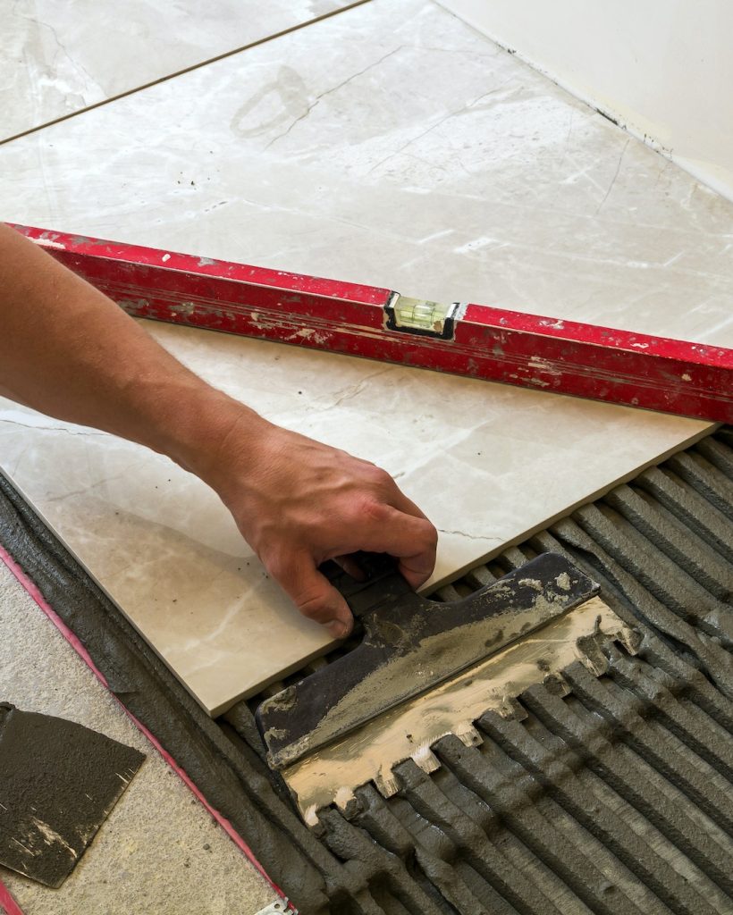 Ceramic tiles and tools for tiler. Worker hand installing floor tiles. Home improvement, renovation