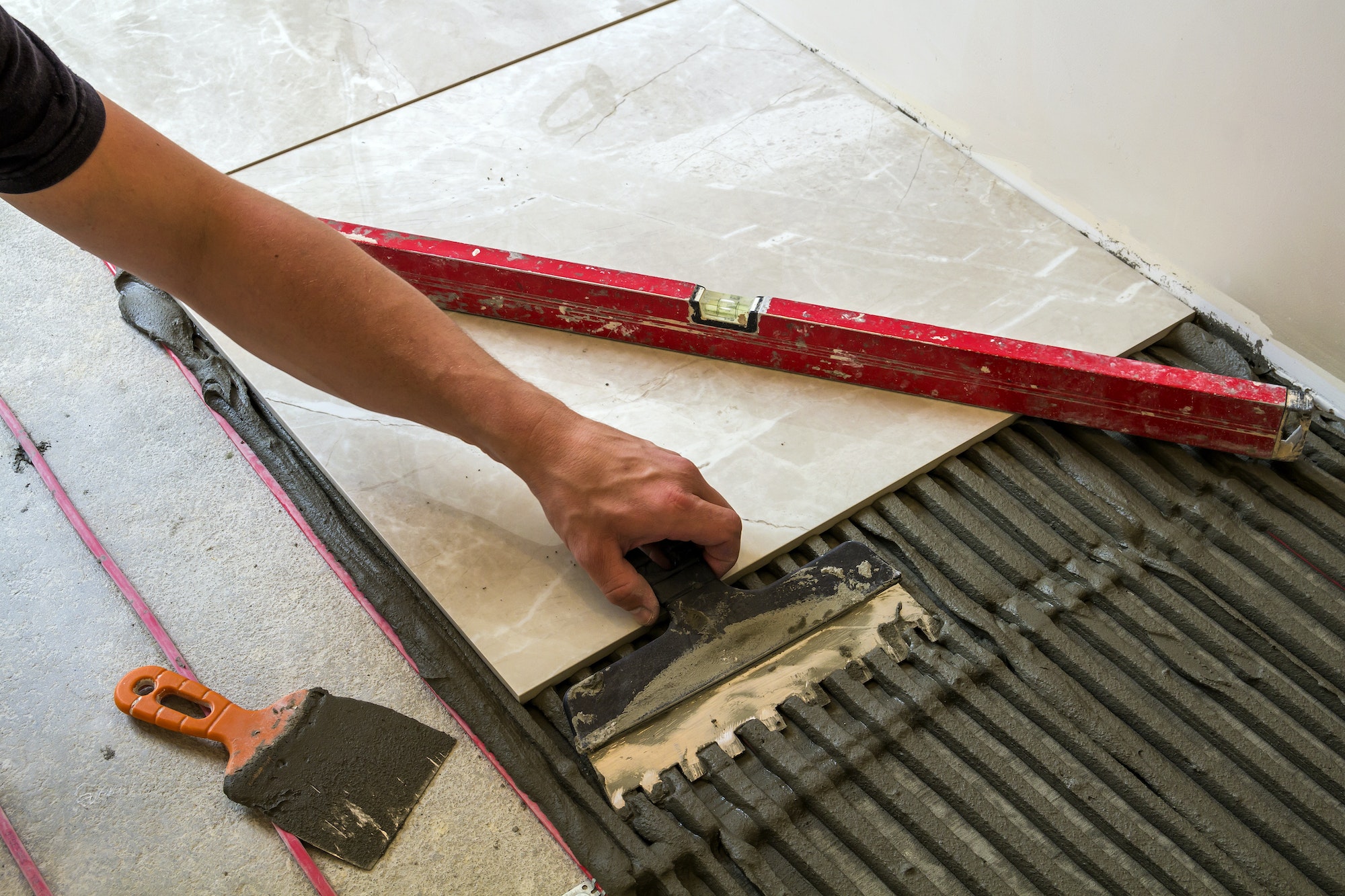 Ceramic tiles and tools for tiler. Worker hand installing floor tiles. Home improvement, renovation